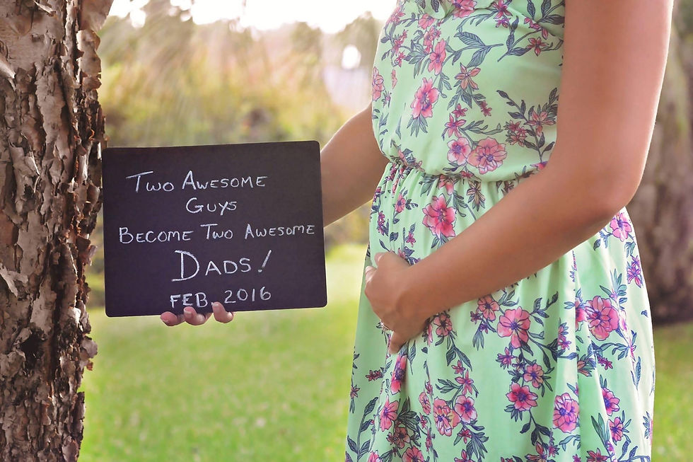 Surrogate holding a sign that says, "Two Awesome Guys Become Two Awesome Dads! Feb 2016"