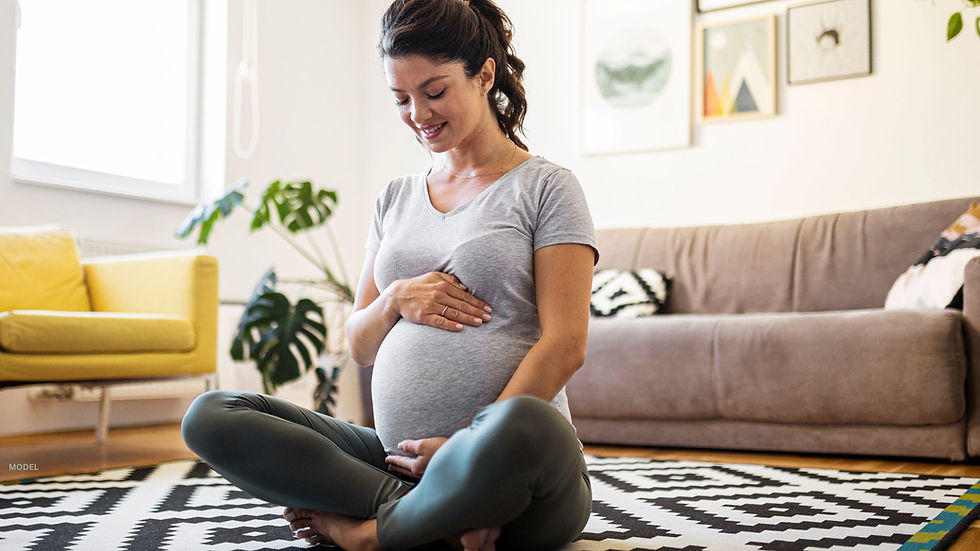 Woman sitting on the floor looking down at her pregnant body