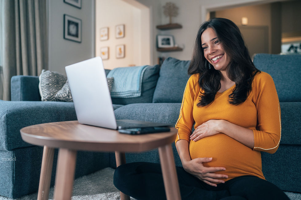 A pregnant woman smiles into her computer screen