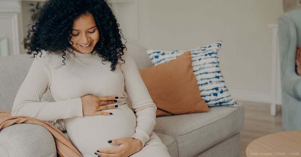 Pregnant woman smiling while looking down with her hands resting on her stomach (model). Source: Getty Images.