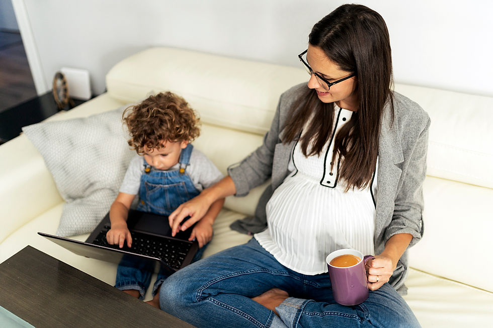 Pregnant mother helping her toddler use a laptop on the couch
