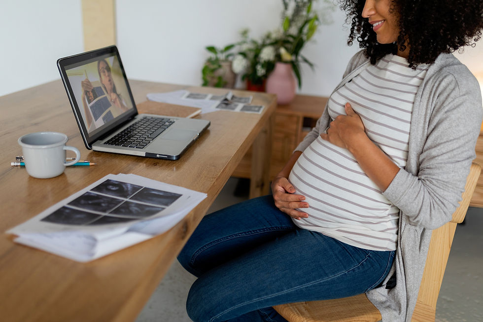 A smiling pregnant woman video chatting with someone at a desk